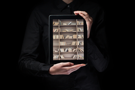 hands holding and showing a tablet pc with library shelves insideの写真素材