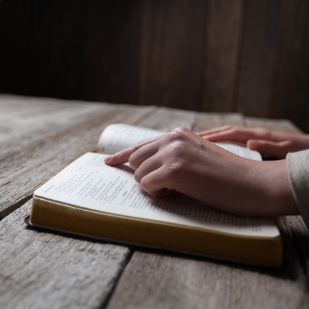 Woman hands praying with a bible in a dark over wooden tableの写真素材