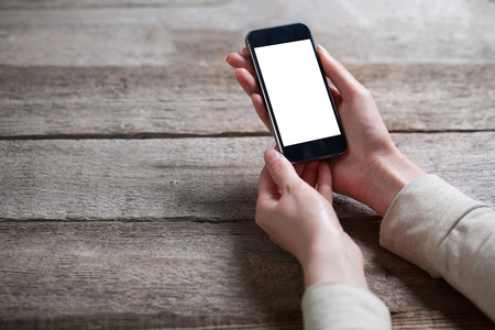 Female hand holding smart phone on wooden backgroundの写真素材