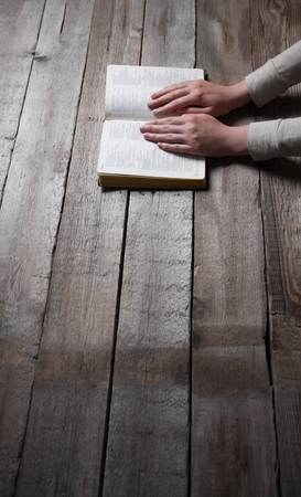 Woman hands praying with a bible in a dark over wooden tableの写真素材