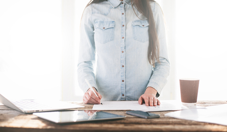 Woman working on a laptop and tablet pc indoor on a wooden standing deskの写真素材