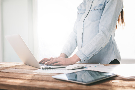 Woman working on a laptop and tablet pc indoor on a wooden standing deskの写真素材