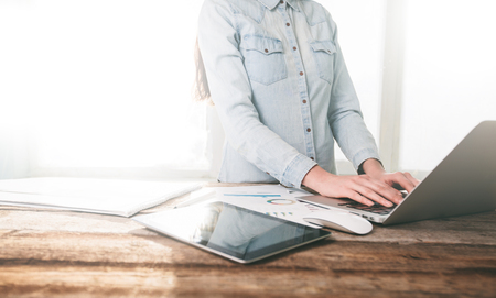 Woman working on a laptop and tablet pc indoor on a wooden standing deskの写真素材