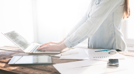 Woman working on a laptop and tablet pc indoor on a wooden standing deskの写真素材