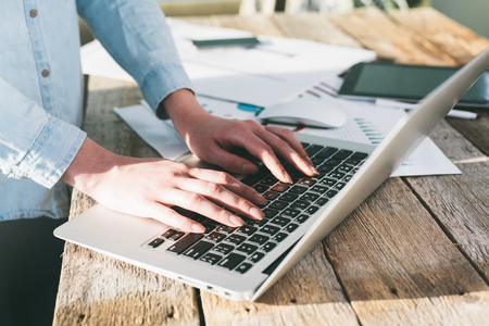 Woman working on a laptop and tablet pc indoor on a wooden standing deskの写真素材