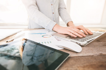 Woman working on a laptop and tablet pc indoor on a wooden standing deskの写真素材