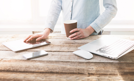 Woman working on a laptop and tablet pc indoor on a wooden standing deskの写真素材