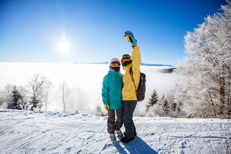 Skiers taking picture of themselves with smartphone over a mountainの写真素材