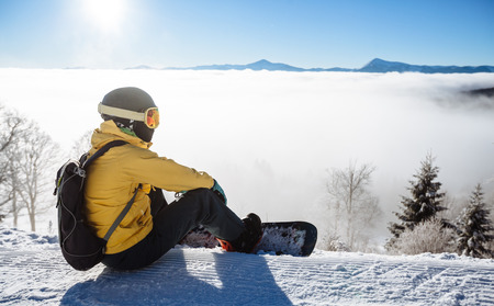 Snowboarder sitting and looking at mountain chain in the backgroundの写真素材
