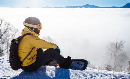 Snowboarder sitting and looking at mountain chain in the backgroundの写真素材
