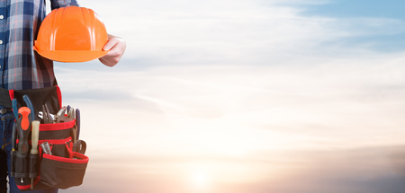 Woman engineer holding a helmet with toolbelt with the sky backgroundの写真素材