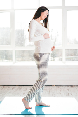 Pregnant woman at home walking and holding bellyの写真素材