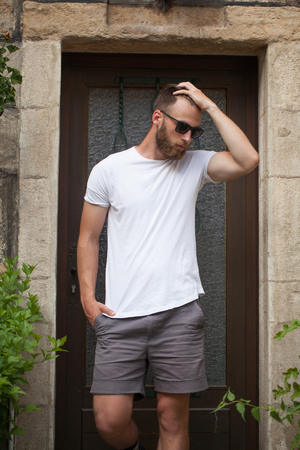 Hipster handsome male model with beard wearing white blank t-shirt with space for your logo or design in casual urban styleの写真素材