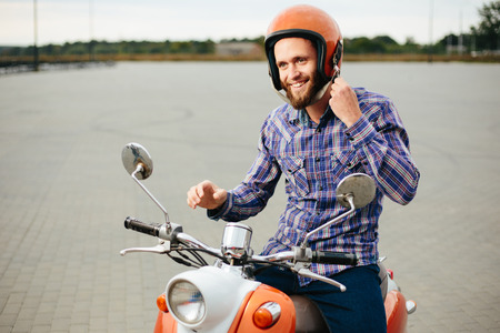 Hipster young  man in helmet is riding on yellow retro scooter in townの写真素材