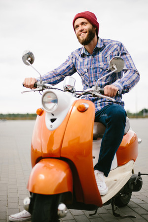 Hipster young  man in helmet is riding on yellow scooter in town.の写真素材
