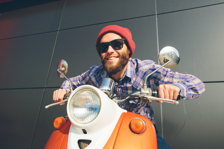 Hipster young  man in helmet is riding on yellow retro scooter in townの写真素材