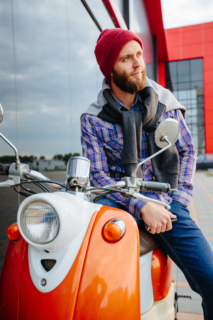 Hipster young  man in helmet is riding on yellow scooter in town.の写真素材