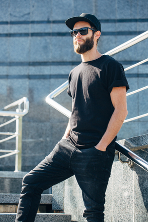 Hipster handsome male model with beard wearing black blank t-shirt with space for your logo or design in casual urban styleの写真素材