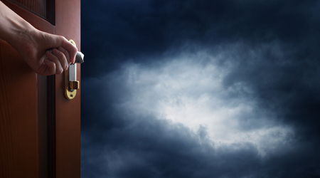 hand opens room door towards a dark skyの写真素材
