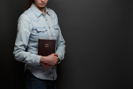 Woman holding a Bible in hands wearing casual clothes over gray backgoundの写真素材