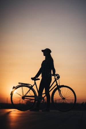 Woman riding a bike in the city during sunsetの写真素材