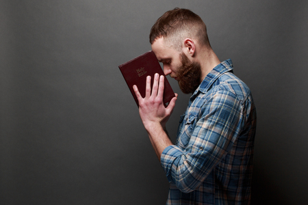 Handsome man reading and praying over Bible in a dark room over gray textureの写真素材