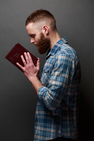 Handsome man reading and praying over Bible in a dark room over gray textureの写真素材