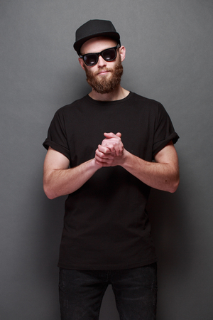 Hipster handsome male model with beard wearing black blank t-shirt with space for your design over gray backgroundの写真素材