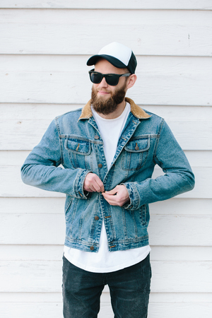 Hipster handsome male model with beard wearing white blank t-shirt and a baseball cap with space for your logo or design in casual urban styleの写真素材