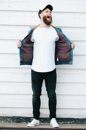 Hipster handsome male model with beard wearing white blank t-shirt and a baseball cap with space for your logo or design in casual urban styleの写真素材