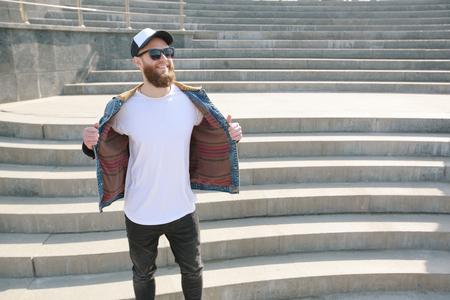 Hipster handsome male model with beard wearing white blank t-shirt and a baseball cap with space for your logo or design in casual urban styleの写真素材