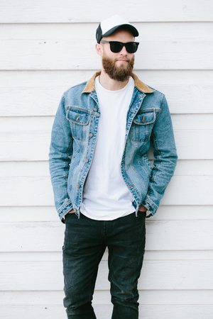 Hipster handsome male model with beard wearing white blank t-shirt and a baseball cap with space for your logo or design in casual urban styleの写真素材