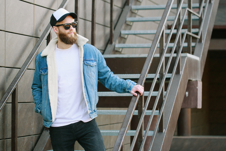 Hipster handsome male model with beard wearing white blank t-shirt and a baseball cap with space for your logo or design in casual urban styleの写真素材