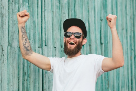 Hipster handsome male model with beard wearing white blank t-shirt and a baseball cap with space for your logo or design in casual urban styleの写真素材