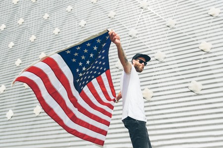 Happy hipster man holding American or USA flag. He is wearing casual clothes.の写真素材