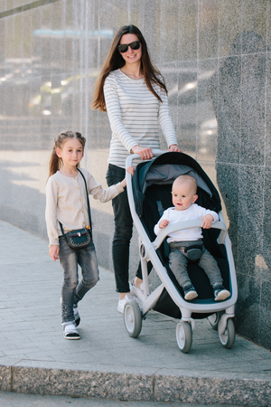 Mother walking with a baby and a stroller in the city streetの写真素材