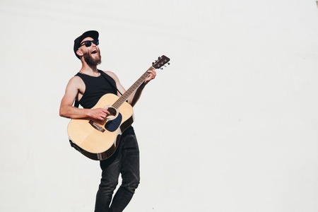 Guitar player singing outside. Hipster guitar player with beard and black clothesの写真素材