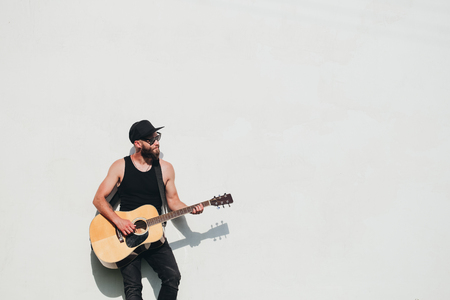 Guitar player singing outside. Hipster guitar player with beard and black clothesの写真素材