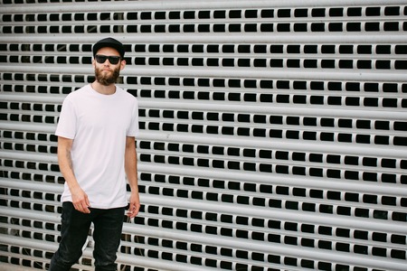 Hipster handsome male model with beard wearing white blank t-shirt and a baseball cap with space for your logoの写真素材