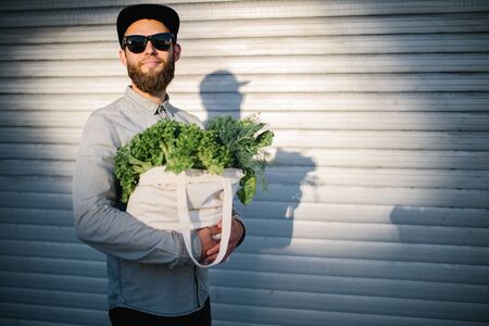 Man holding an eco bag filled with grocery. Vegetables and fruits are hanging from the bag. Ecology concept of environment protectionの写真素材