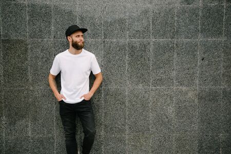 Hipster handsome male model with beard wearing white blank t-shirt and a baseball cap with space for your logo or design in casual urban styleの写真素材