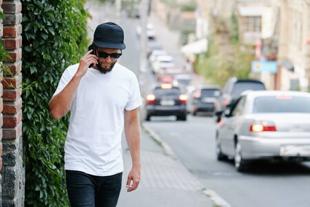 Hipster handsome male model with beard wearing white blank t-shirt and a baseball cap with space for your logo or design in casual urban styleの写真素材