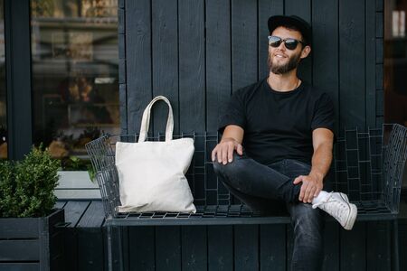 Young man holding white textile eco bag against urban city background. . Ecology or environment...