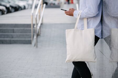 Young man holding white textile eco bag against urban city background. . Ecology or environment protection concept. White eco bag for mock up.の写真素材