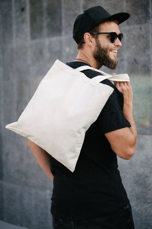 Young man holding white textile eco bag against urban city background. . Ecology or environment protection concept. White eco bag for mock up.の写真素材