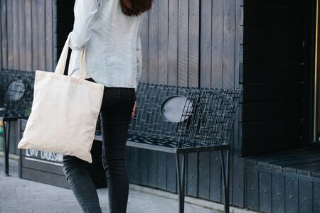 Woman holding white textile eco bag against urban city background. Ecology or environment protection concept. White eco bag for mock up.の写真素材