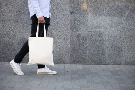 Young man holding white textile eco bag against urban city background. Ecology or environment...