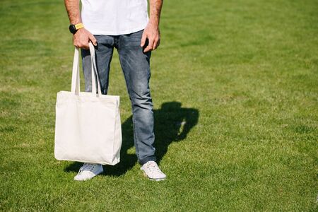 Young man holding white textile eco bag against urban city background. Ecology or environment protection concept. White eco bag for mock up.の写真素材