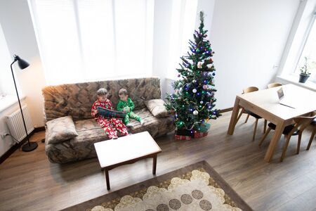 Children are reading a book next to a christmas tree wearing pajamasの写真素材