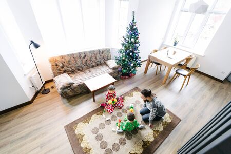 Children with mother playing indoors next to a christmas treeの写真素材
